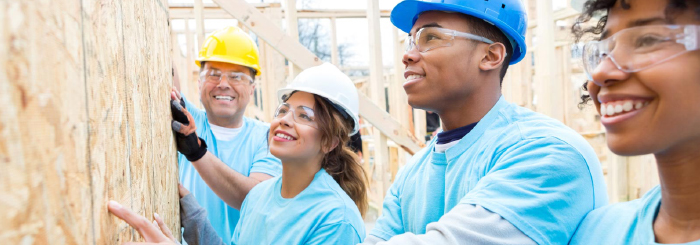 Group of smiling volunteers building a home for the community Group of smiling volunteers building a home for the community