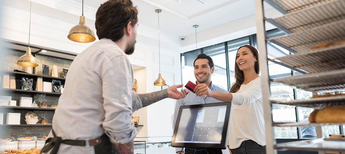 Happy couple handing their credit card to cashier for merchant service 