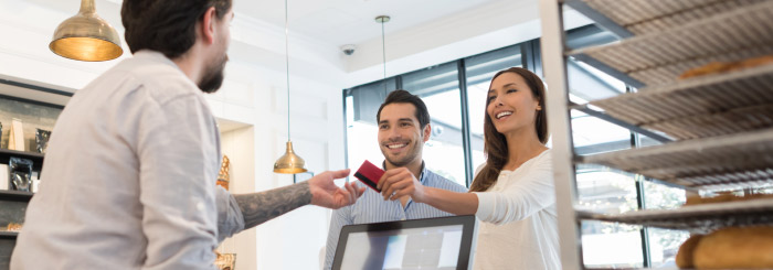 Happy couple handing their credit card to cashier for merchant service Happy couple handing their credit card to cashier for merchant service