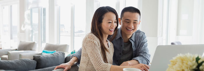 Smiling couple looking at laptop for foreign currency accounts transactions