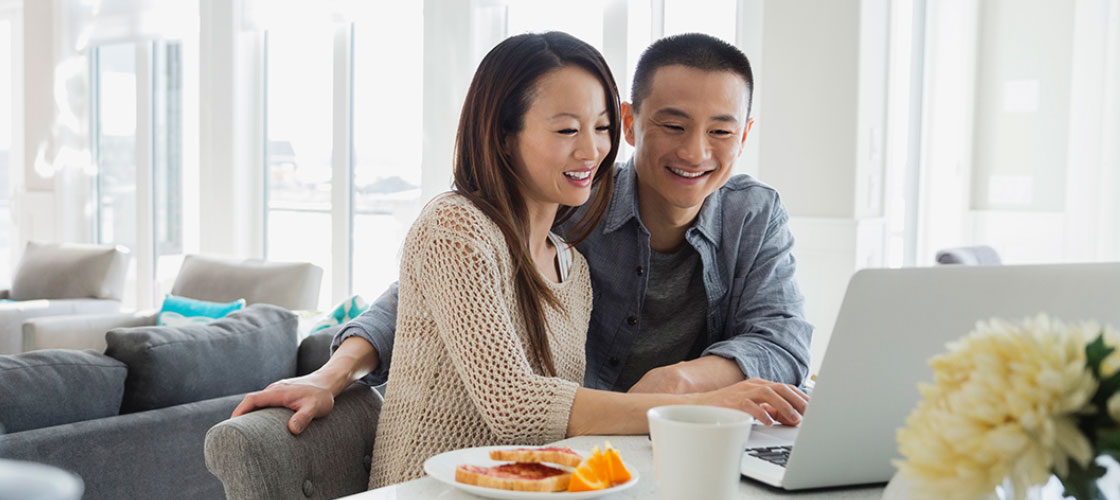 Smiling couple looking at laptop for foreign currency accounts transactions