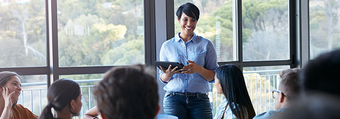 Smiling female teacher holding tablet in classroom with students Smiling female teacher holding tablet in classroom with students