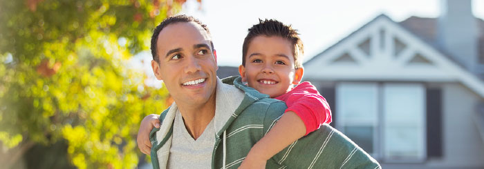 Smiling father carrying his son on his back in front of home Smiling father carrying his son on his back in front of home