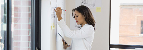 Small business owner working on her tablet device and sketching on a blueprint 