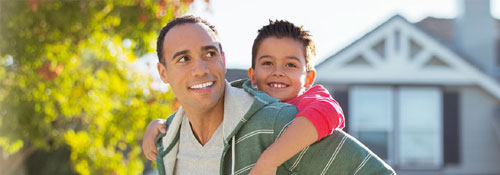 Smiling father carrying his son on his back in front of home