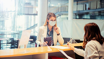 Female customer in face mask talking to banker bank counter Female customer in face mask talking to banker bank counter
